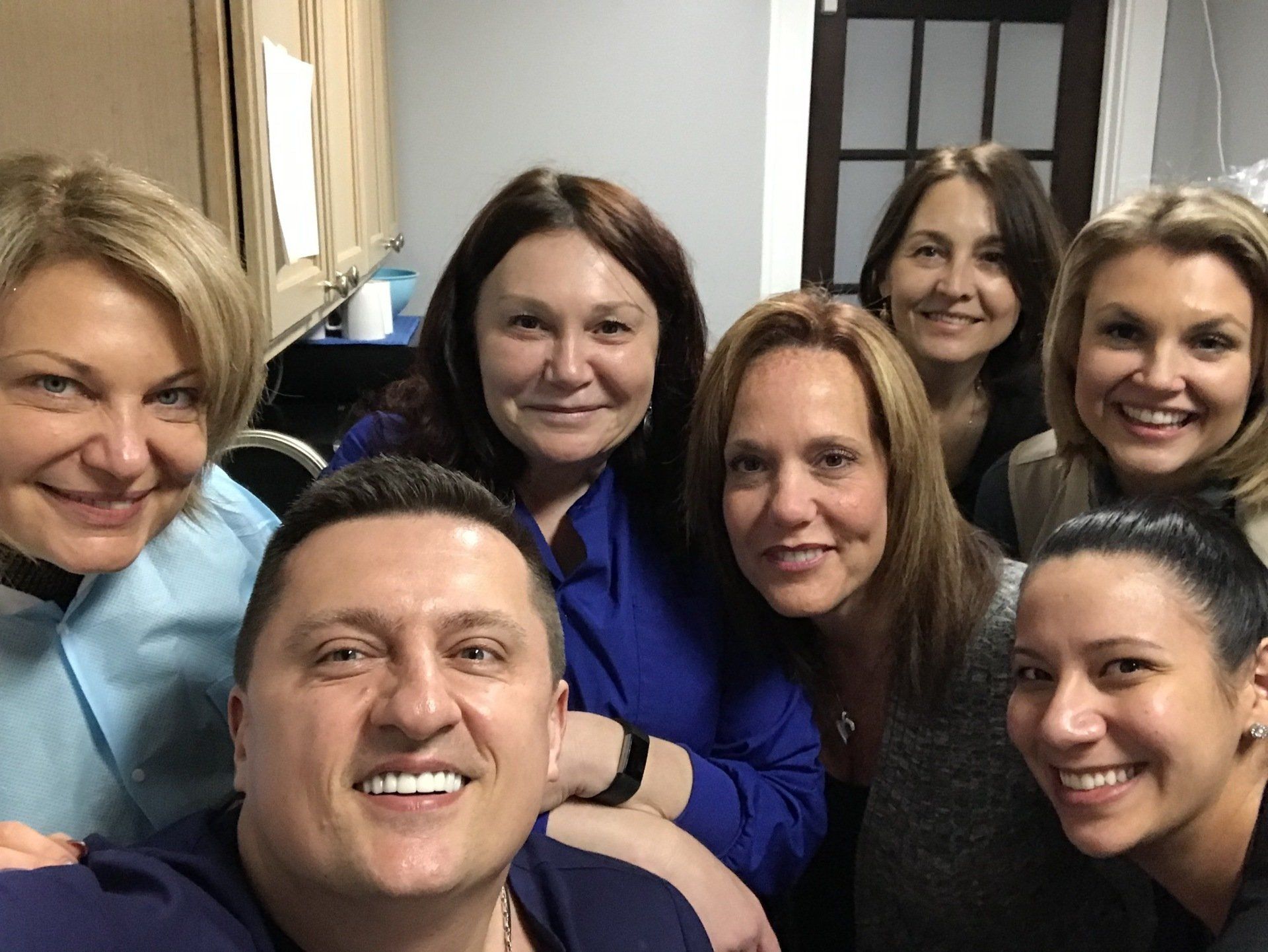 Group selfie: smiling dental staff in a neutral-toned office.