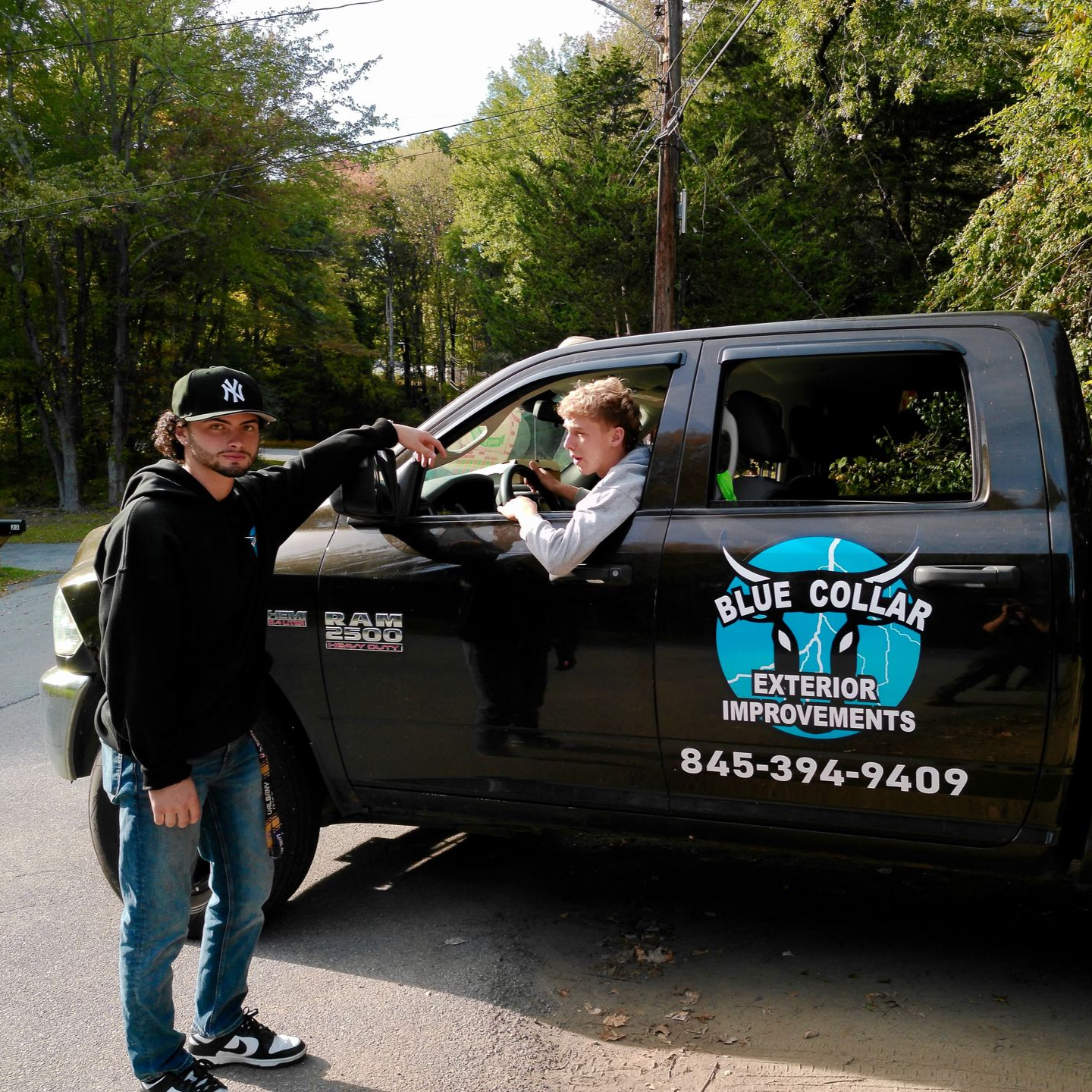 Two men by a black work truck. One points to the driver. Truck has