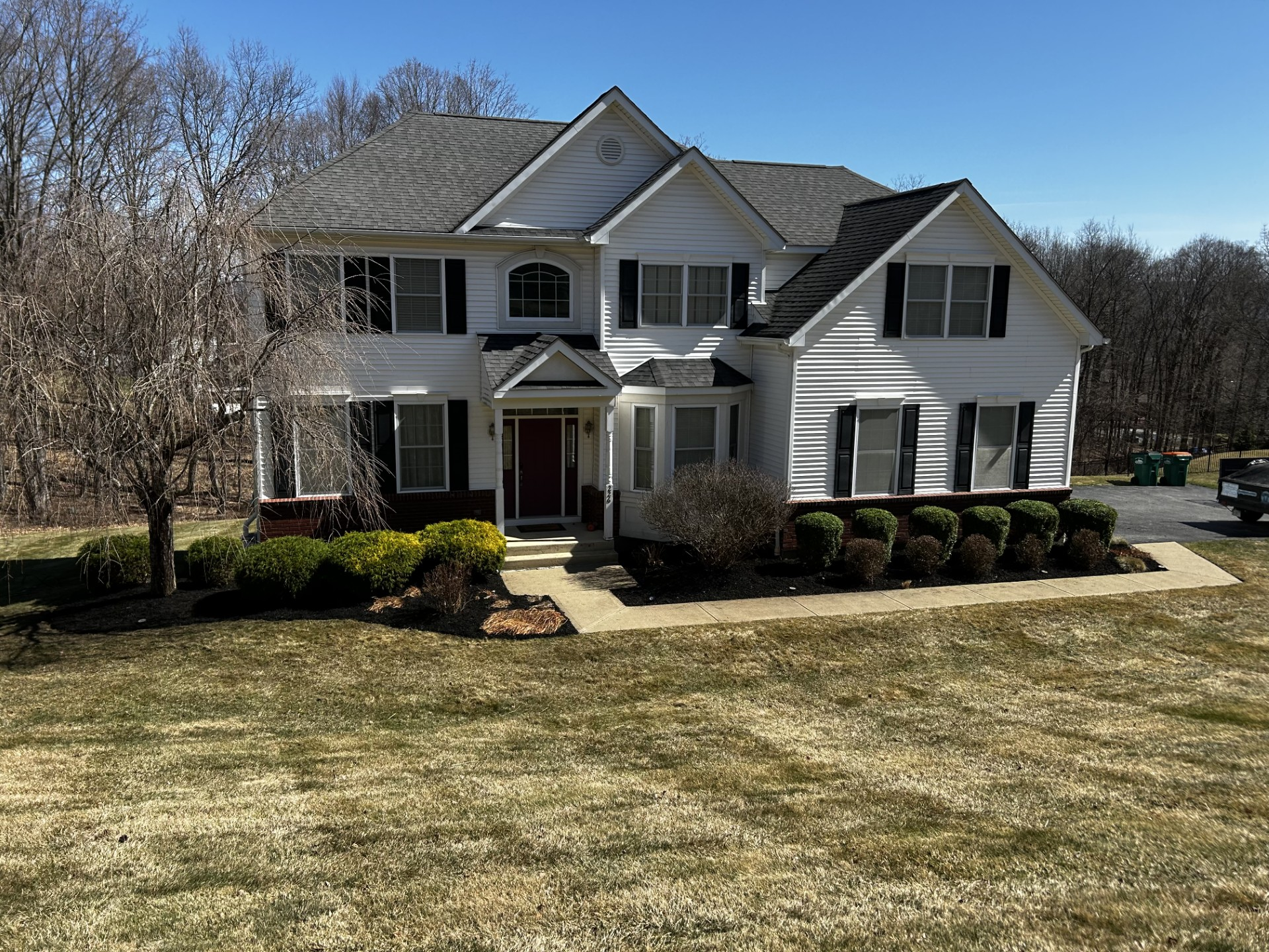 White two-story house with black shutters, red front door, and manicured lawn. Sunny day.