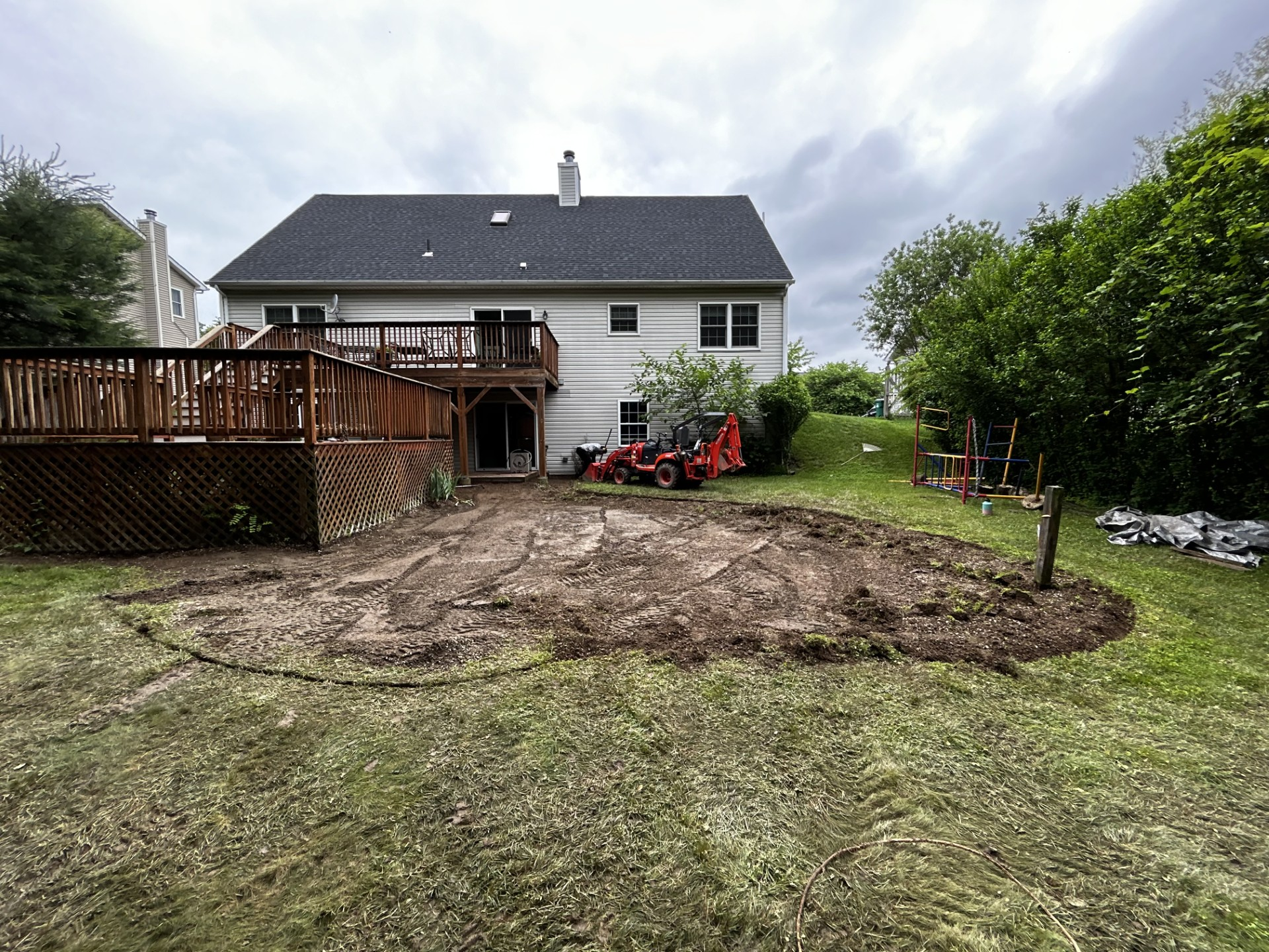 Backyard with a deck, excavated area in the middle, and a house under an overcast sky.