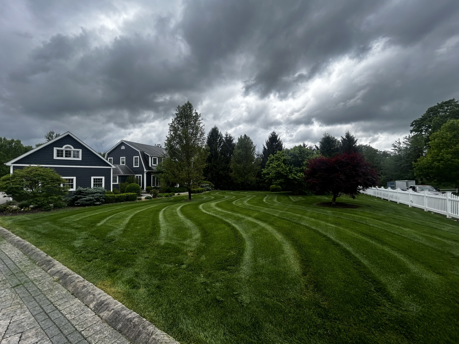Green lawn with curved mowing lines, dark house, stormy sky.