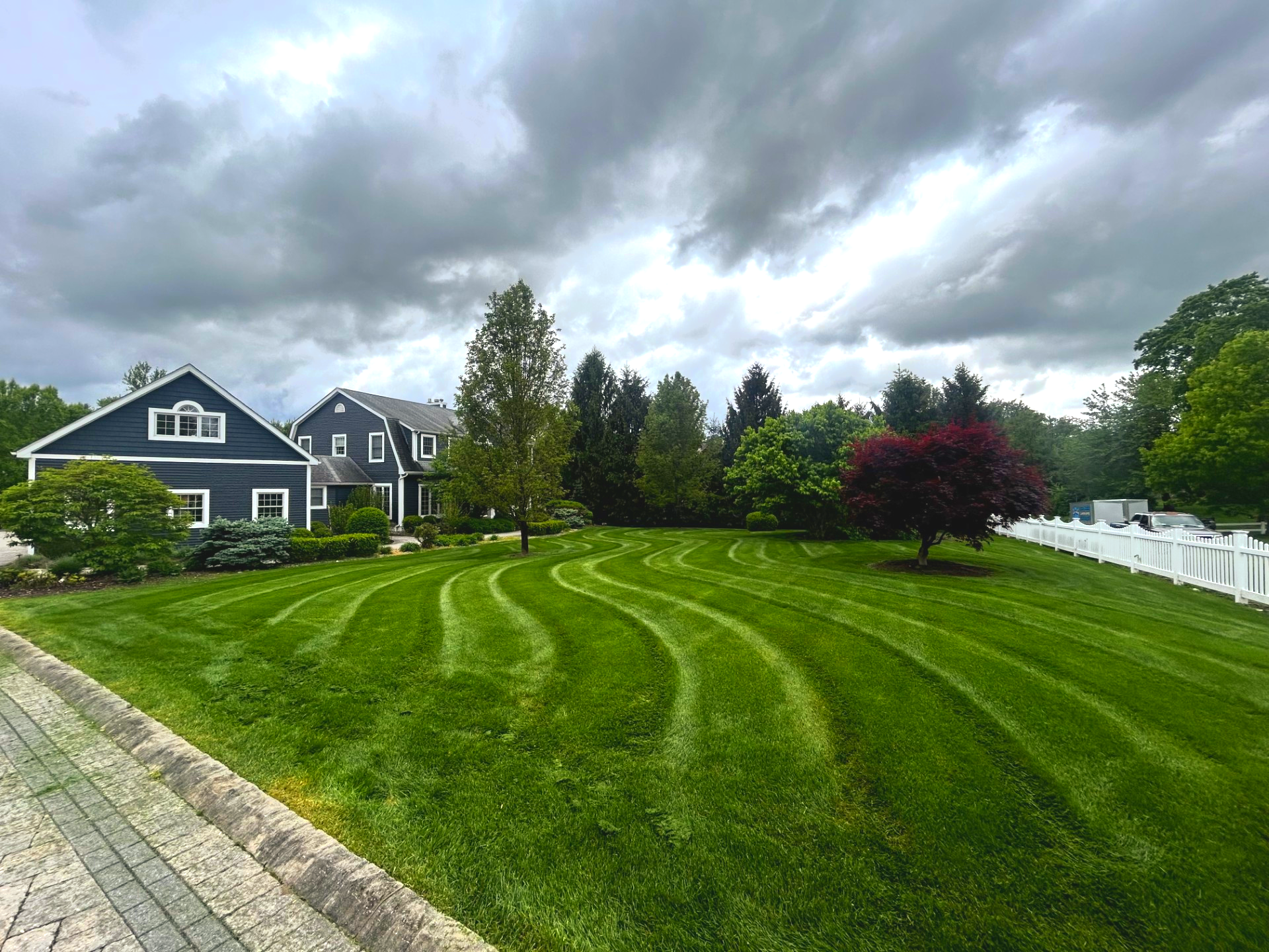 Lawn mowed in curved patterns in front of a blue house under a cloudy sky.