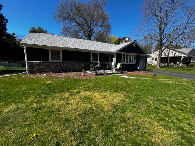 Ranch-style house with dark siding and a light-colored roof.  Green lawn in front.