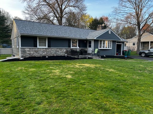 Ranch-style house with blue siding, stone facade, and gray roof, surrounded by green grass.