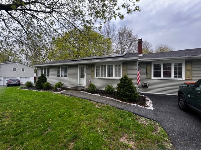 Gray ranch house with green lawn, driveway, and American flag; cloudy sky.