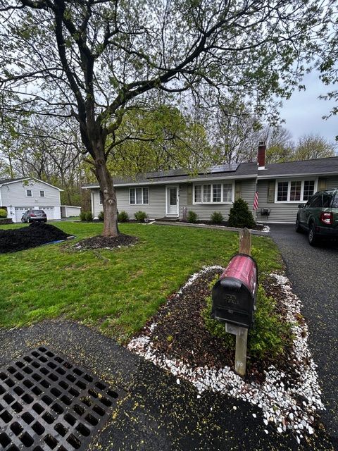 A ranch-style house with a lawn, driveway, mailbox, and a tree in front. Overcast sky.