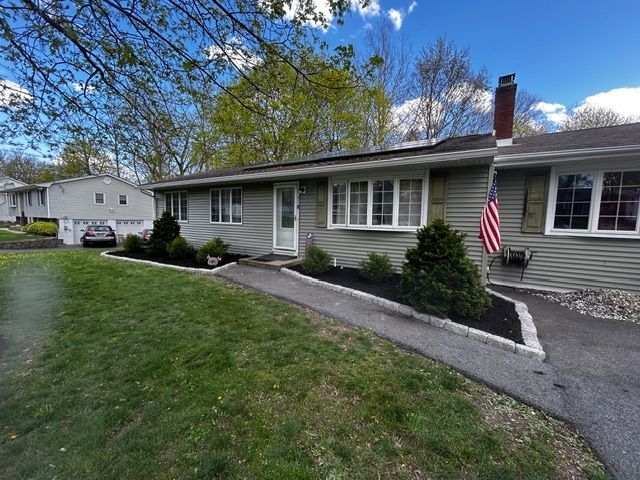 Green house with front yard, walkway, black mulch beds, and American flag.