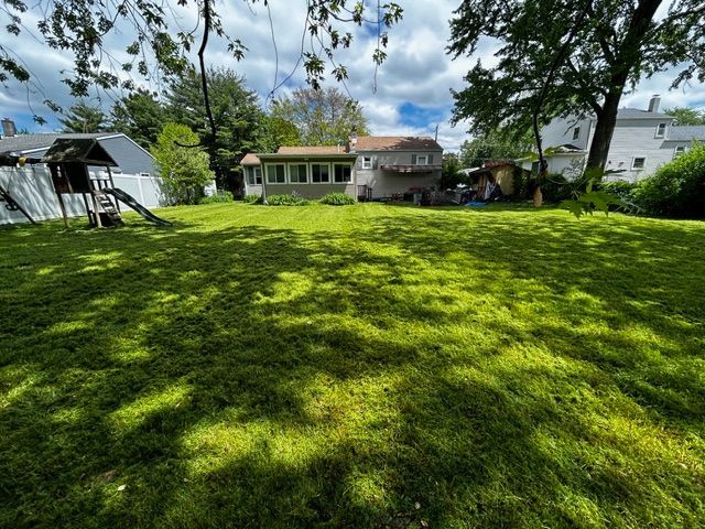 Green, grassy backyard with a house, trees, and a small play structure on a sunny day.