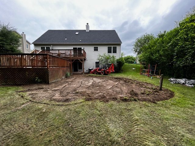 Backyard landscaping: a house with a deck, excavated dirt area, and lawn under cloudy skies.