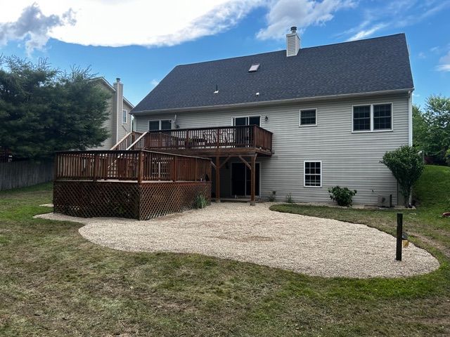 Back of a house with a multi-level wooden deck and a gravel patio in the backyard.