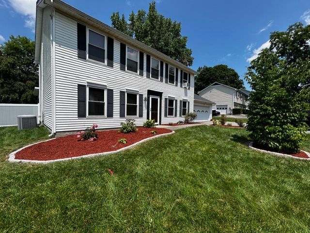 White two-story house with black shutters, red mulch landscaping, and green lawn on a sunny day.
