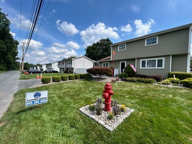 A two-story house with green siding, a red fire hydrant, and a truck parked in the driveway on a cloudy day.