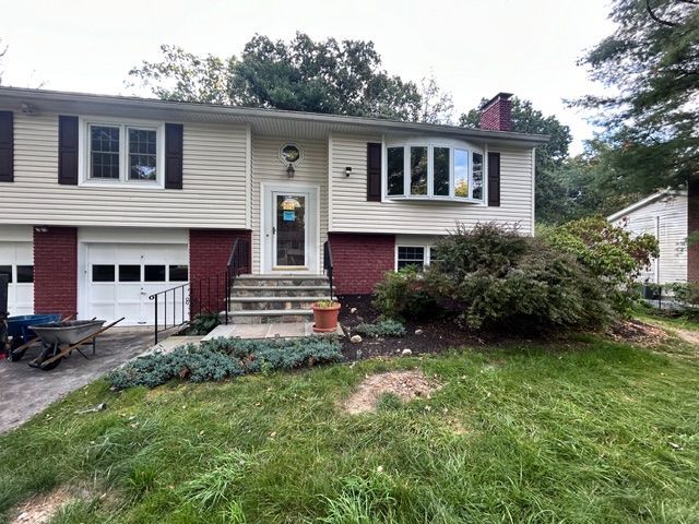 Split-level house with red brick accents, tan siding, bay window, and a small garden.