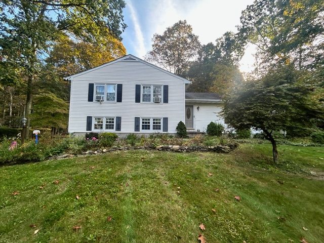 White two-story house with black shutters, set on a green lawn with fall foliage backdrop.
