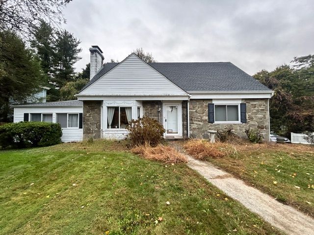 Small stone house with a dark roof and a walkway leading to the front door on a cloudy day.
