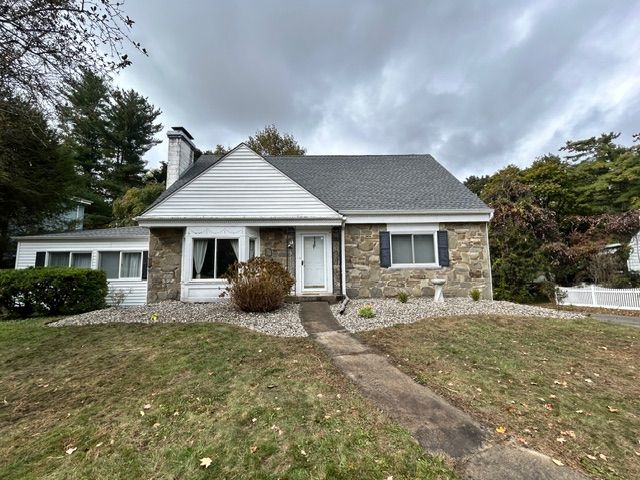 Stone-faced bungalow house with white trim, gray roof, and a cloudy sky background.