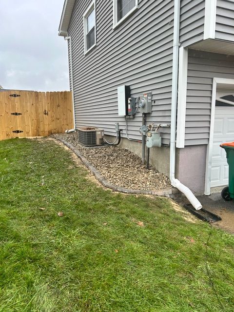 Exterior view of a house with a fence, lawn, and gravel landscaping around an AC unit and utility boxes.