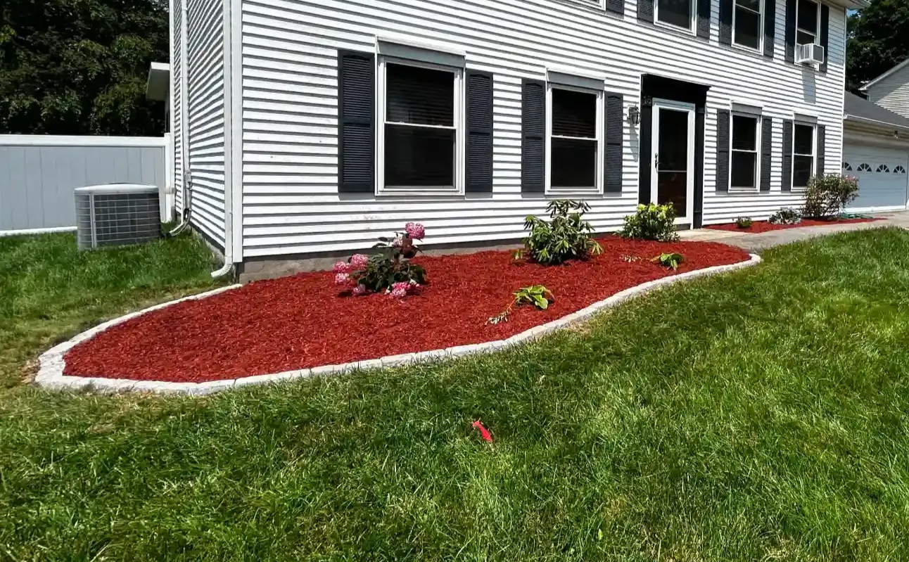 Two men stand in front of a snow plow attached to a truck. They are smiling and have their arms crossed. Autumn leaves are in the background.