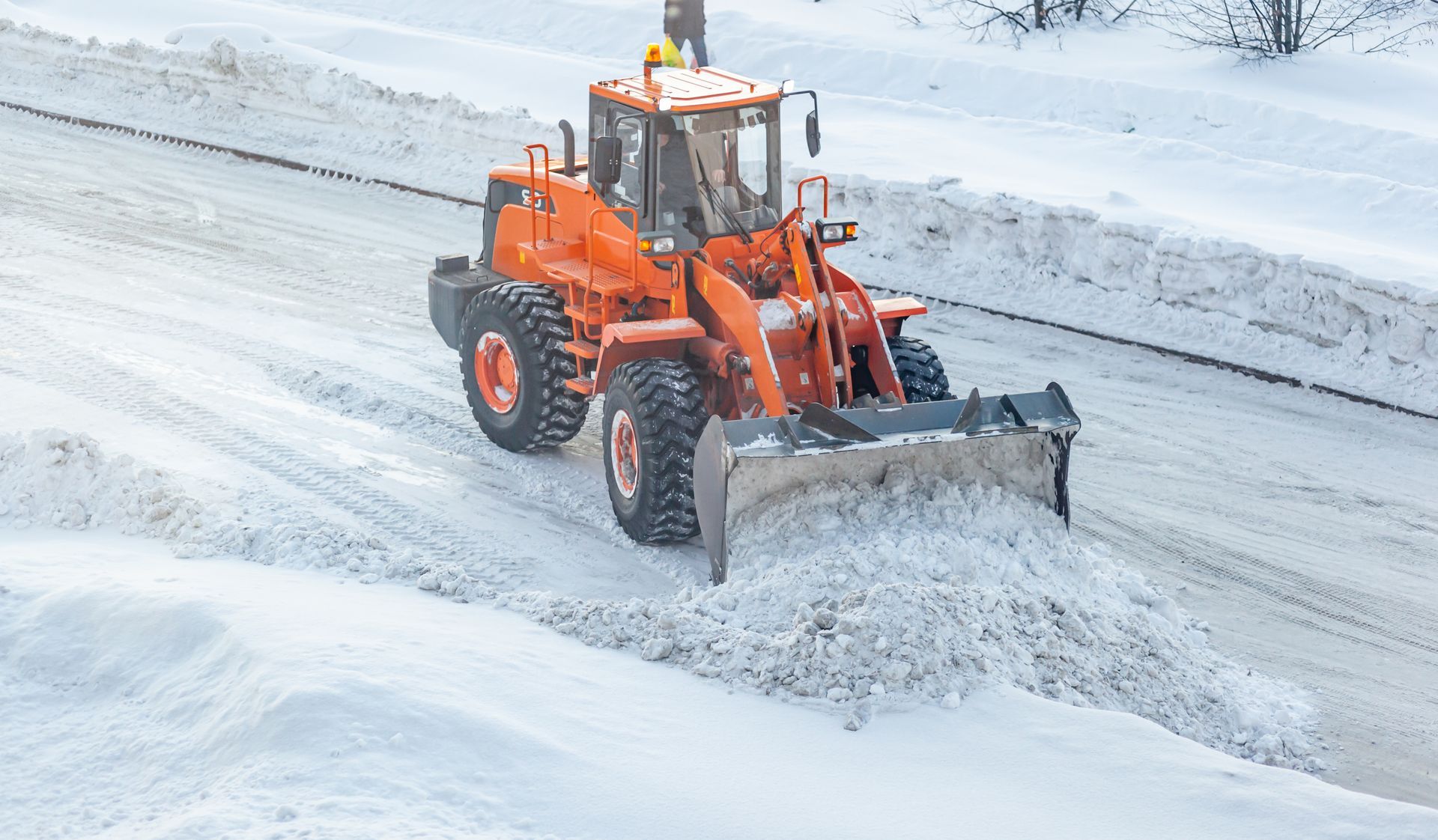Orange snowplow clearing snow from a road on a snowy day.