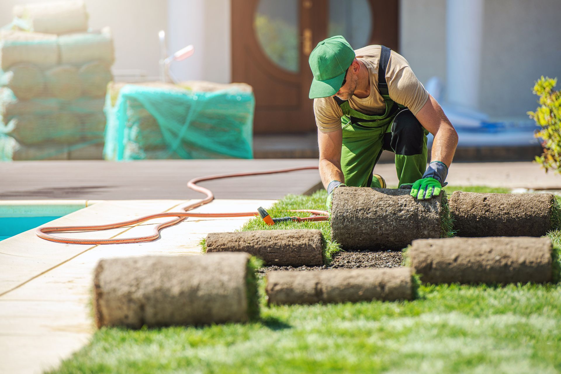 Worker laying rolled sod on a lawn beside orange hose in a sunny yard