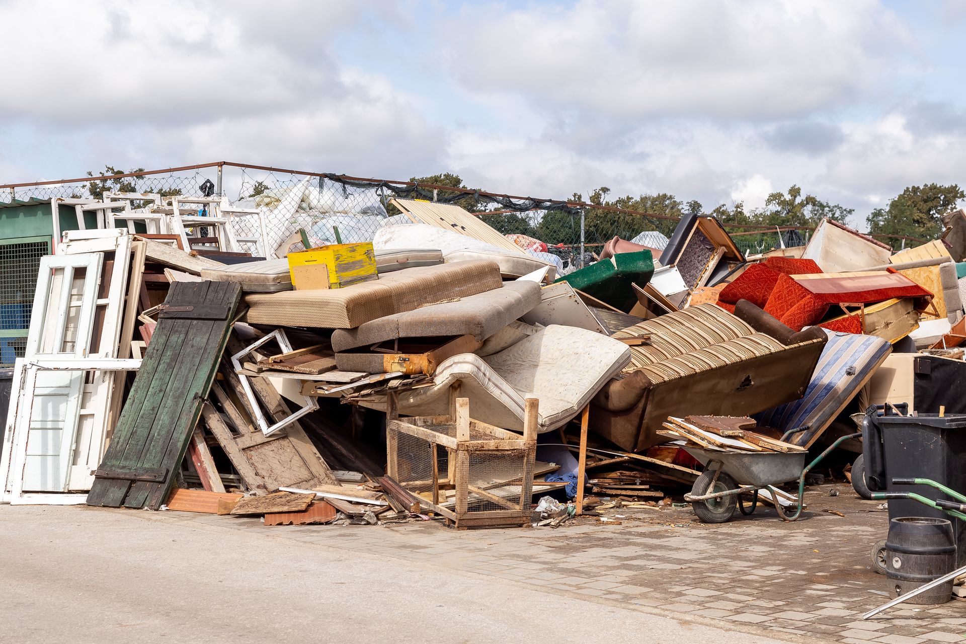 Pile of discarded furniture and construction debris at a waste disposal site under a cloudy sky.