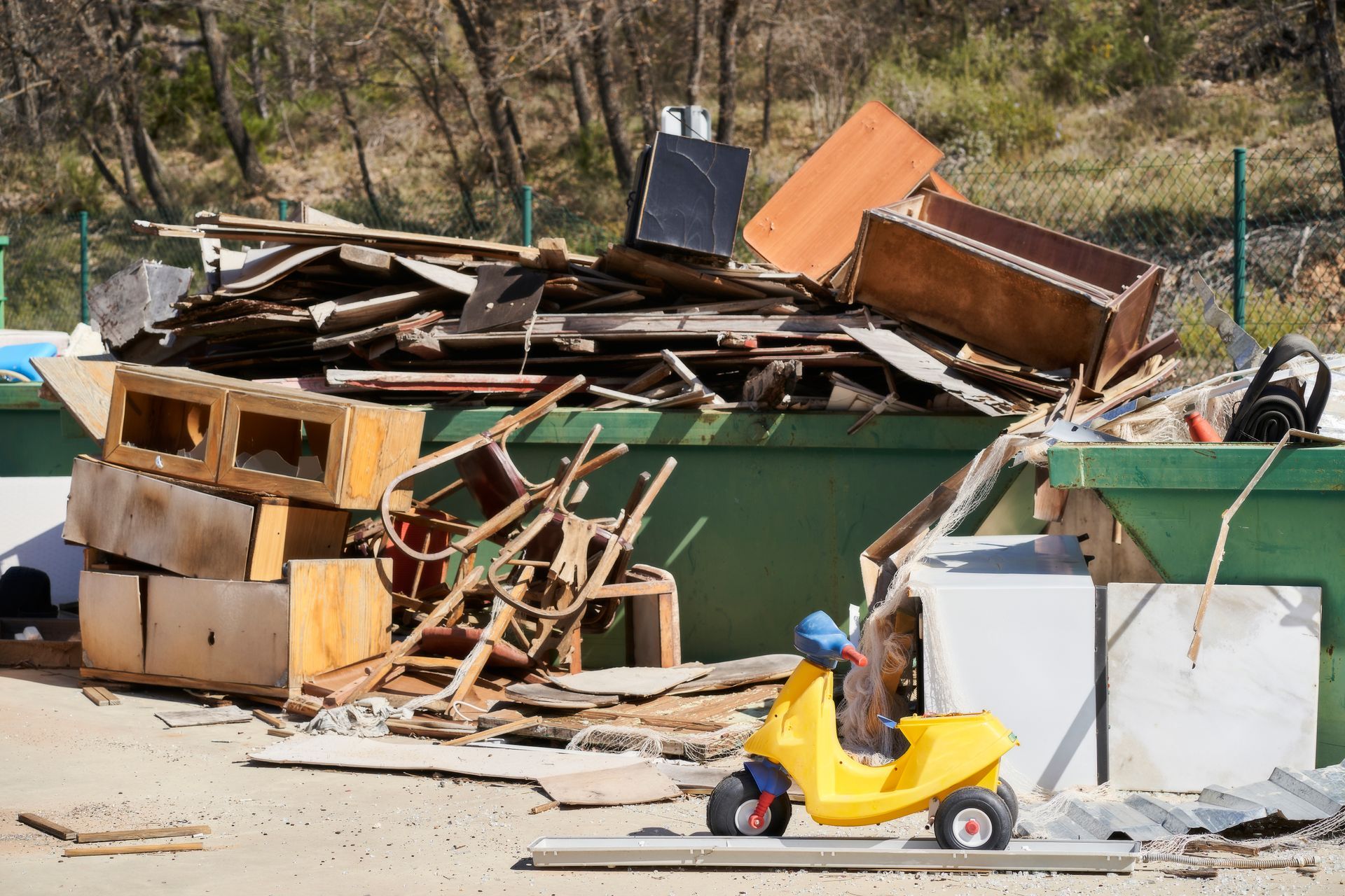 A dumpster overflowing with discarded wood, furniture, and a yellow toy scooter.