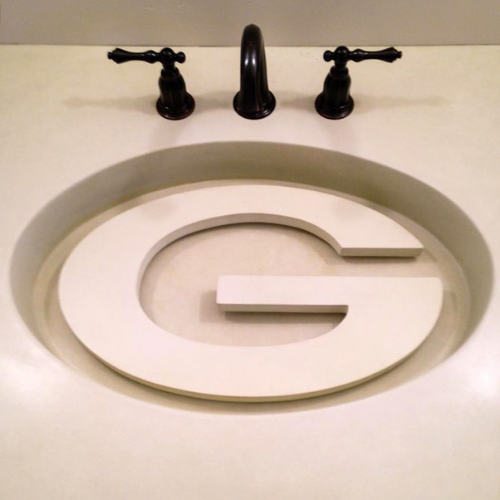 A concrete bathroom sink with the letter g on it.