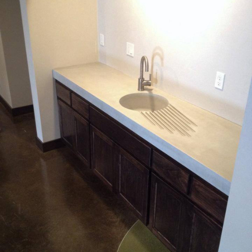 A concrete kitchen counter with a sink and wooden cabinets