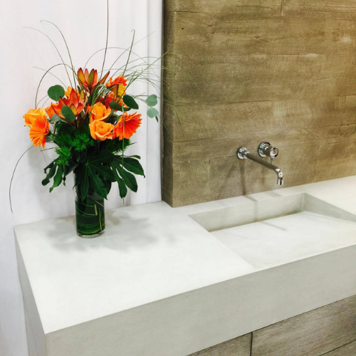 A vase of flowers sits on a concrete counter next to a sink