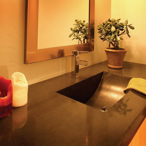 A concrete bathroom sink with two potted plants and a mirror