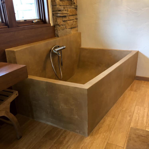 A concrete bathtub in a bathroom next to a window