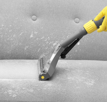 Yellow-gloved hand using a vacuum nozzle to clean a gray sofa covered in lint and dust