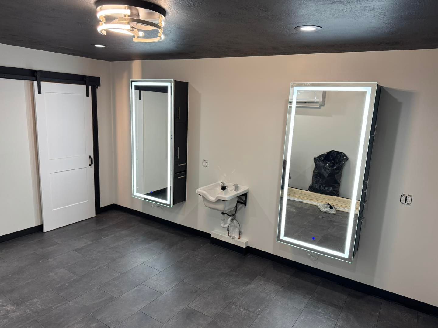 Woman and man smile close together. Woman has long brown hair, man wears a tan jacket. Dim lighting, indoor setting.