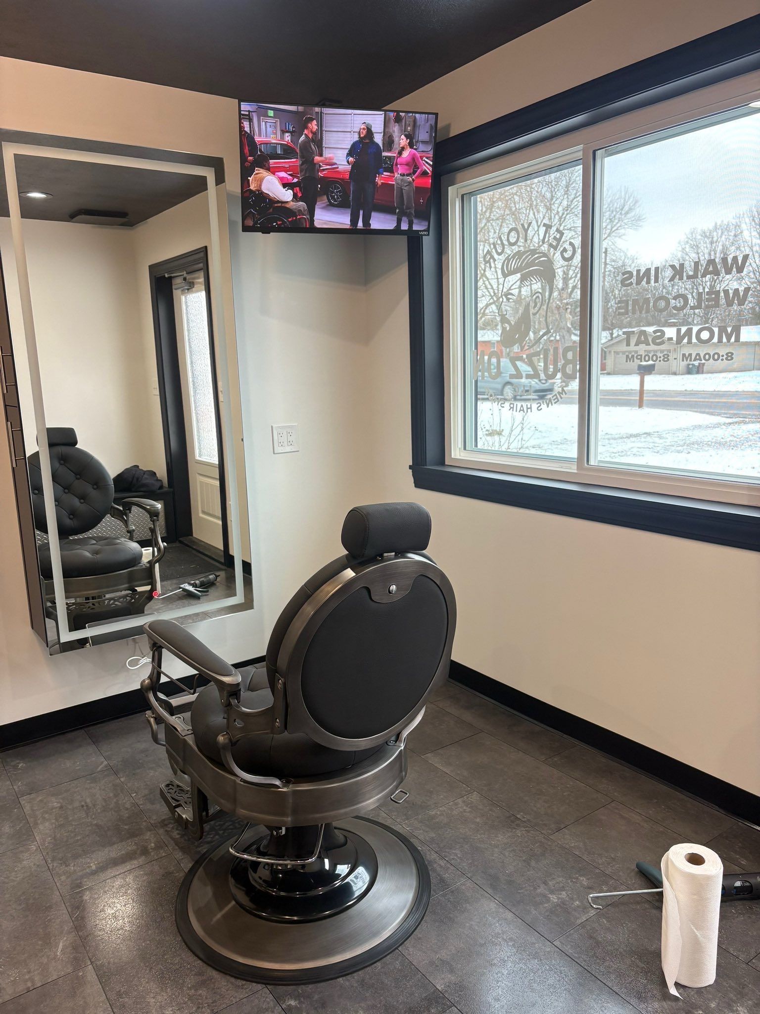 Barber shop interior with chair, mirror, TV, and window showing a snowy scene.