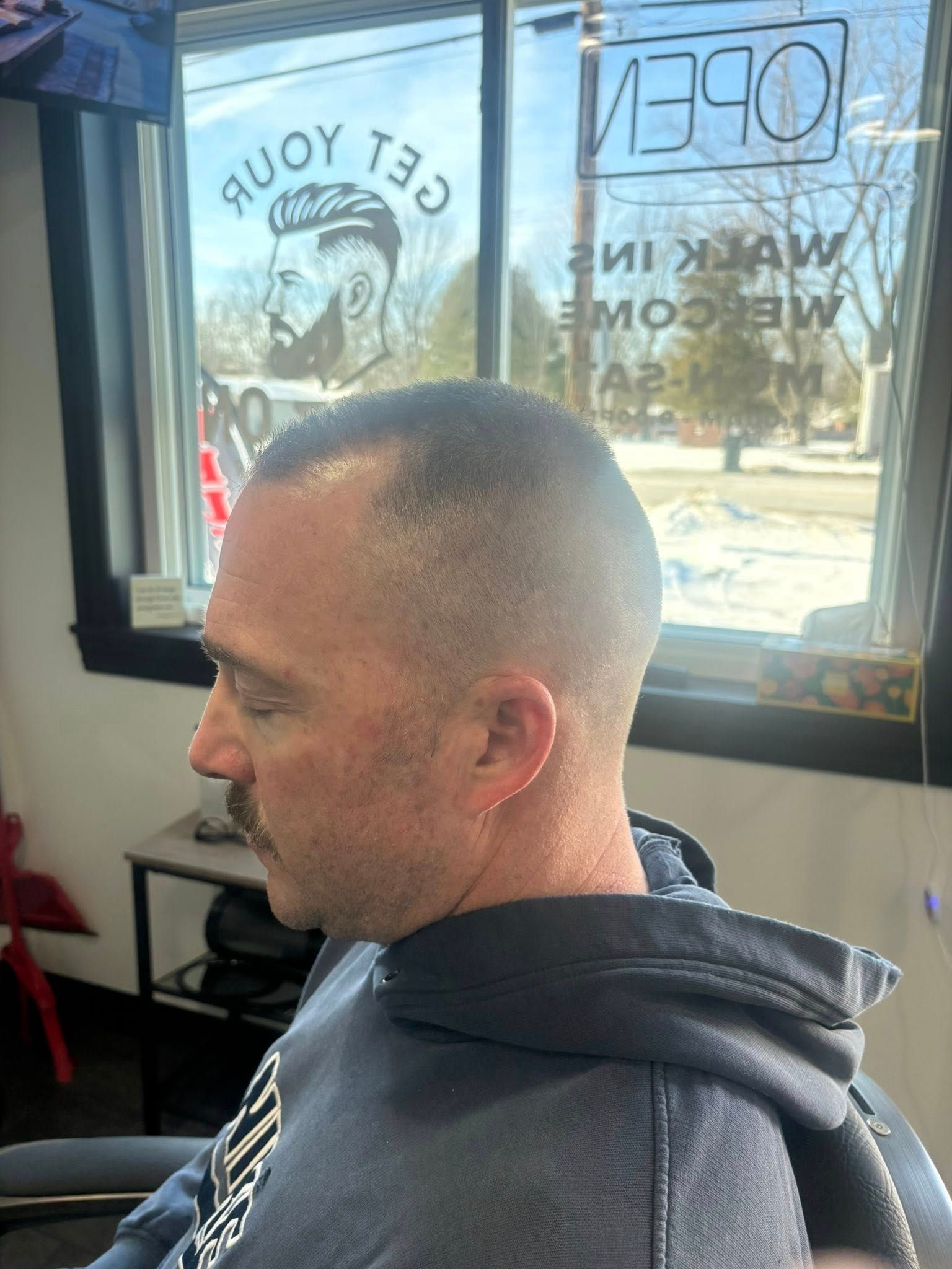 Man with a short haircut in a barber chair.  A window with 