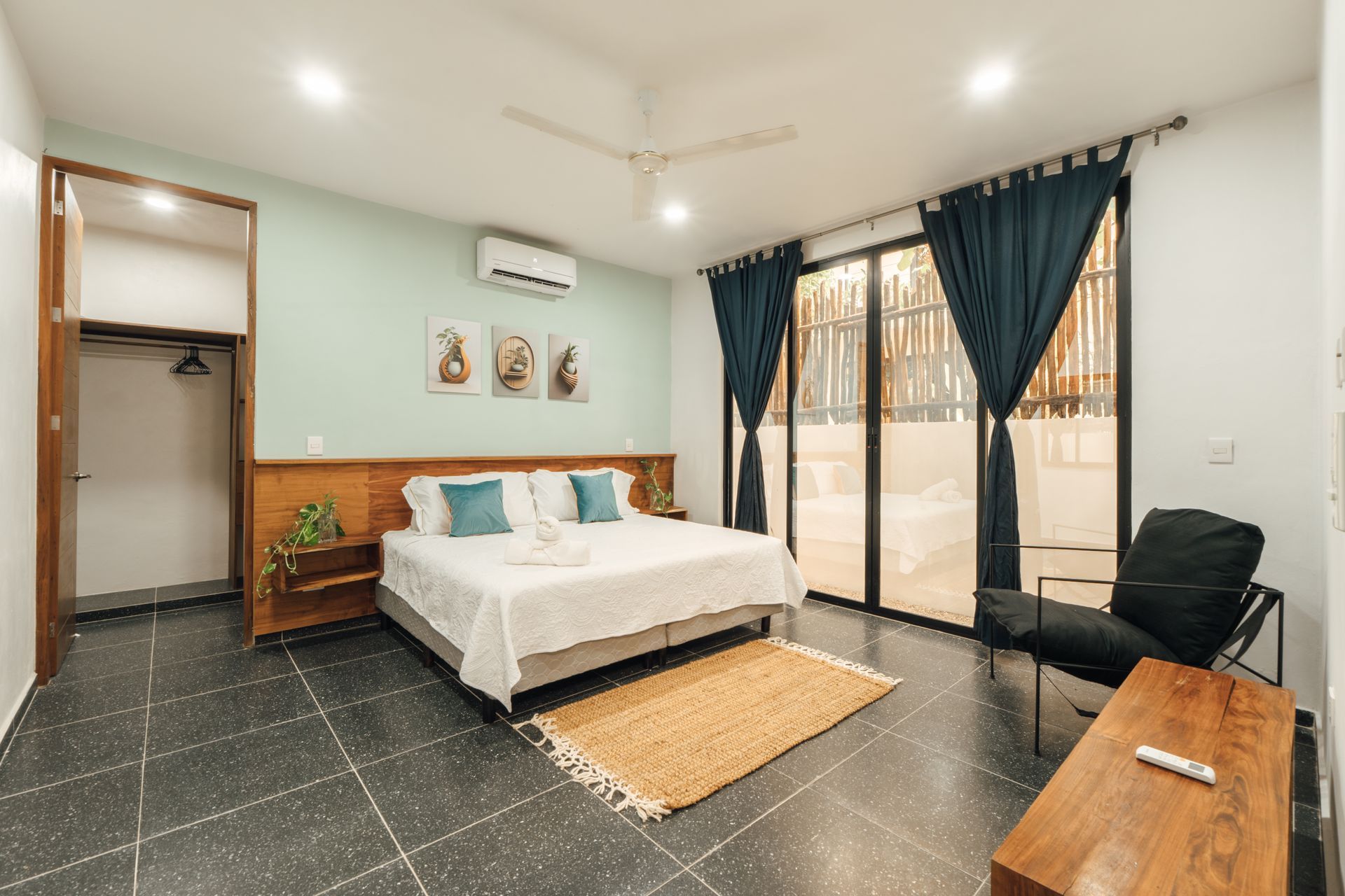Bedroom with king bed, blue accents, sliding glass door to outside, black tile floor, and a chair.