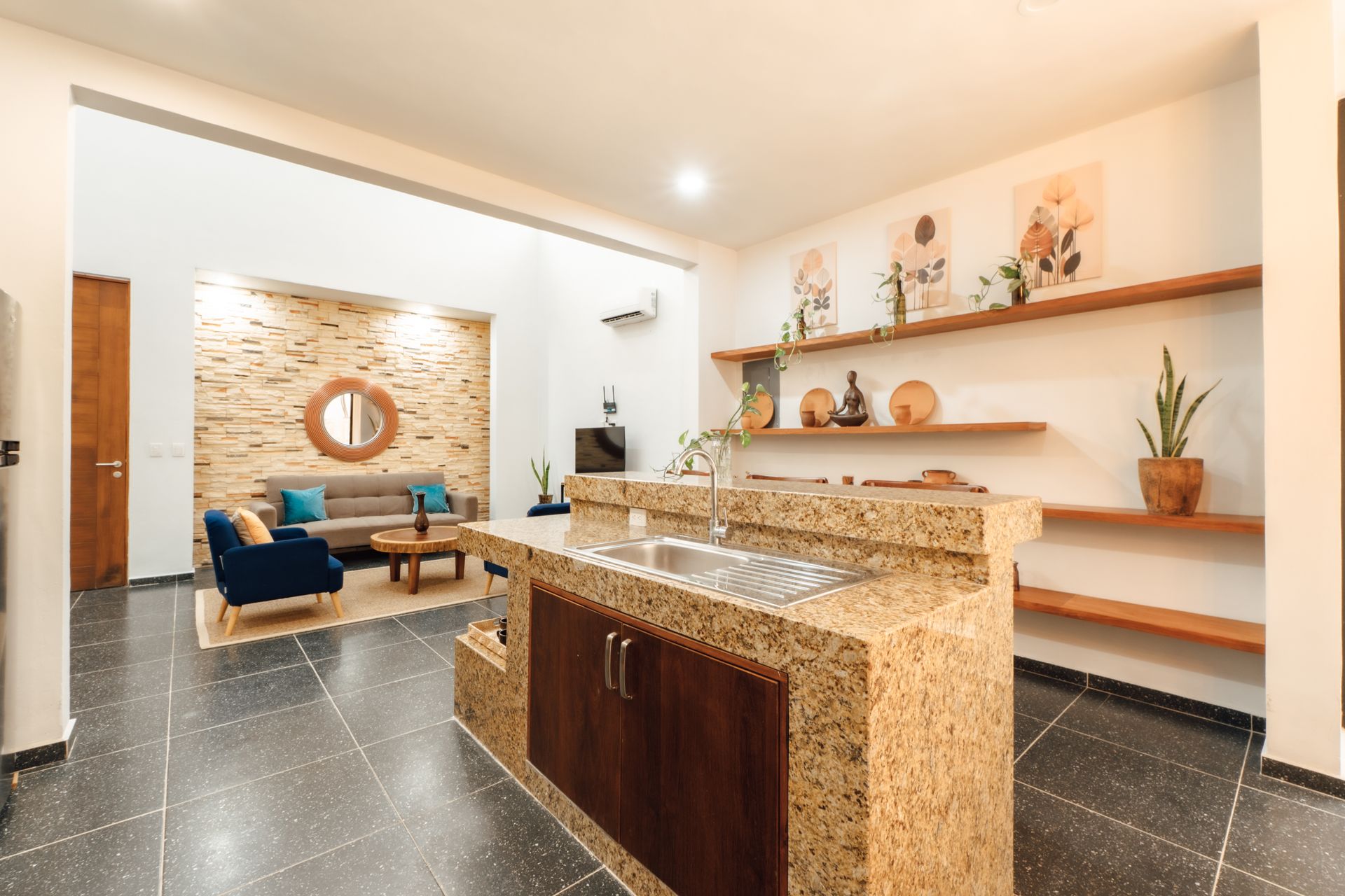 Open-concept living space with a kitchen island and a living room visible in the background, neutral colors.