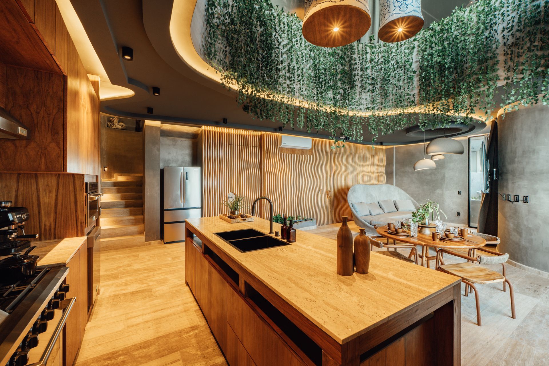 Luxurious open-plan kitchen with wooden island, stone walls, and hanging plants from the ceiling.