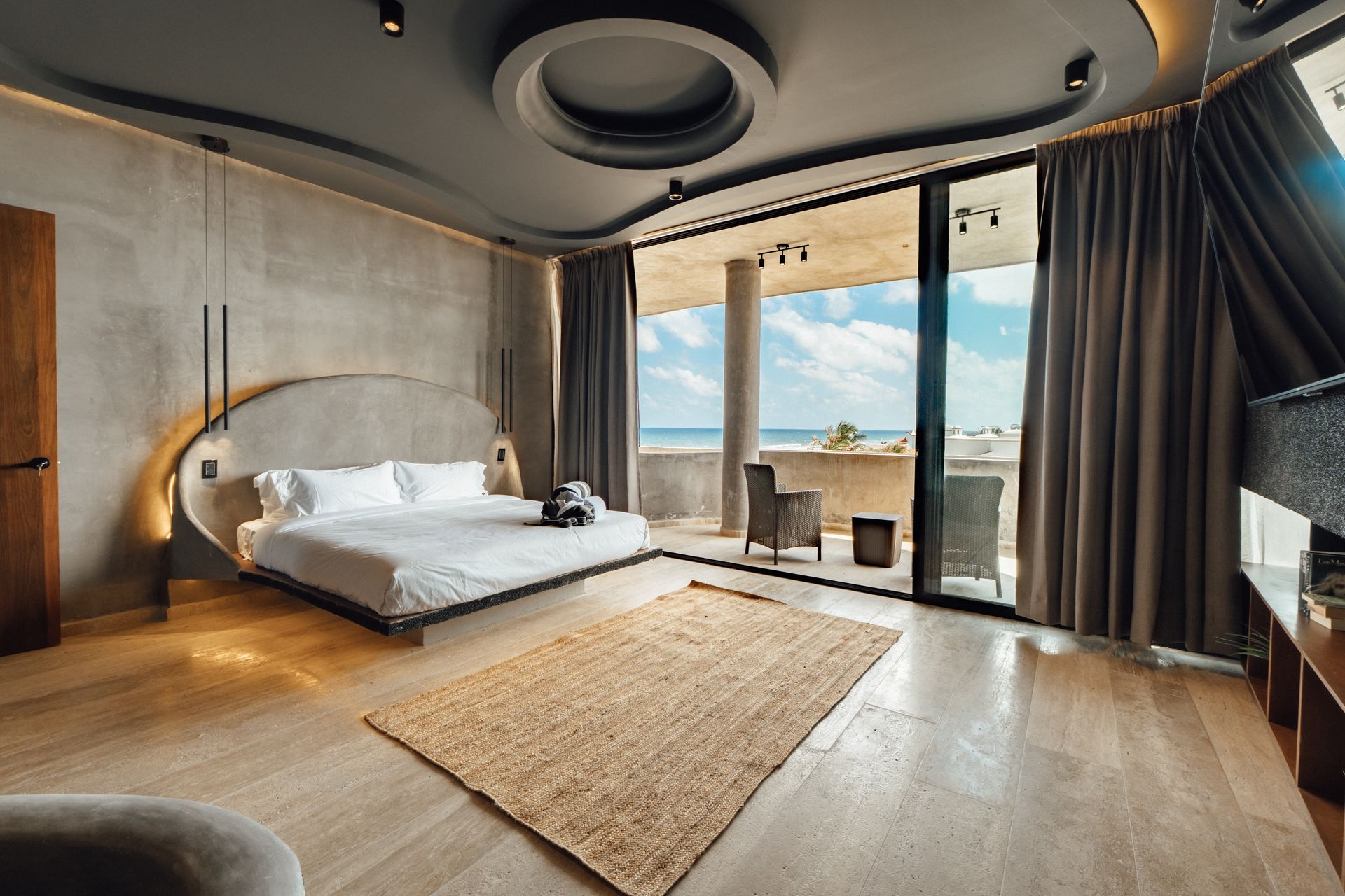 Modern bedroom with a bed, ocean view, and neutral tones.
