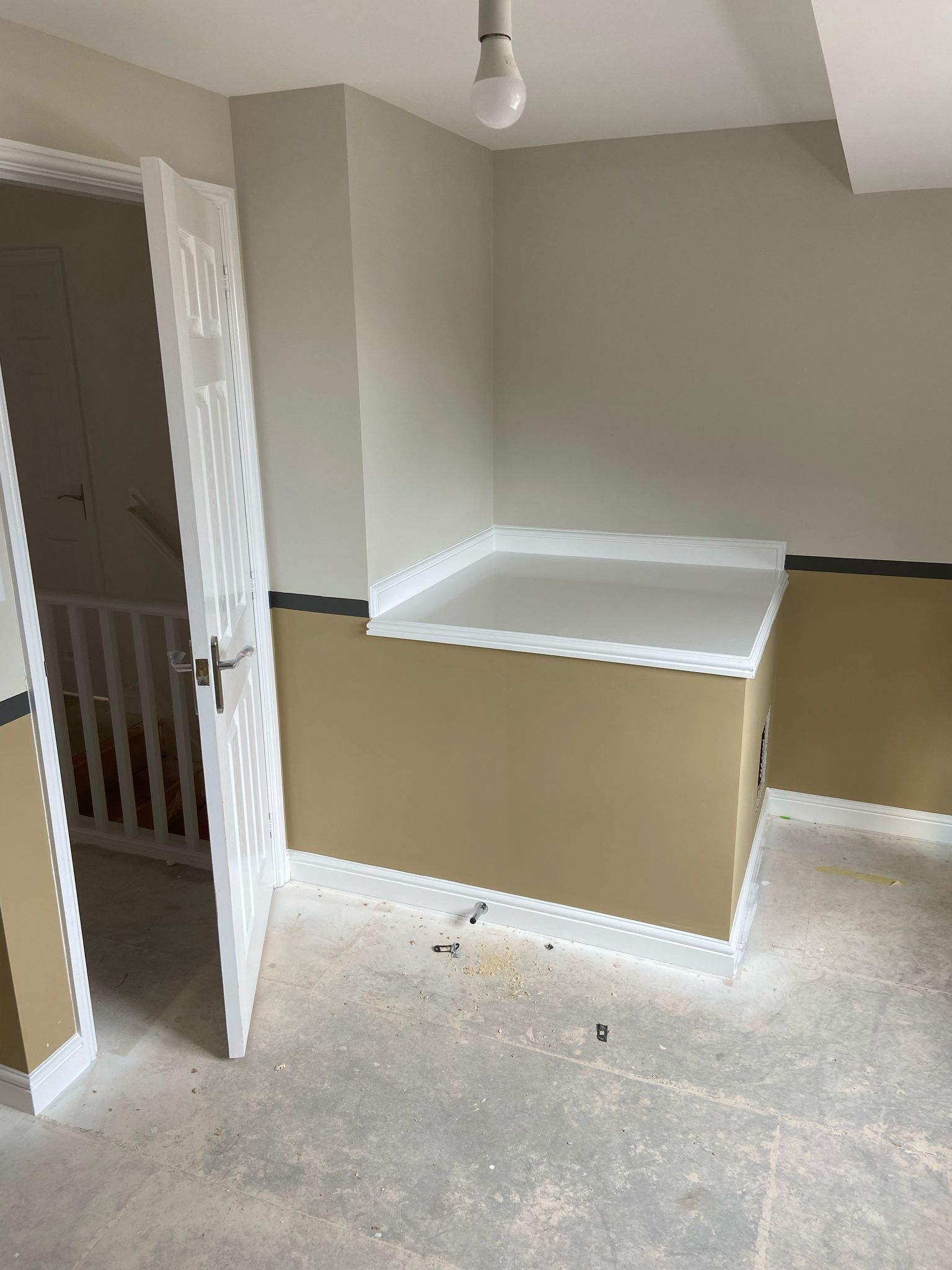 Empty room with partially constructed ledge and open door. Beige and tan walls, white trim and baseboard.