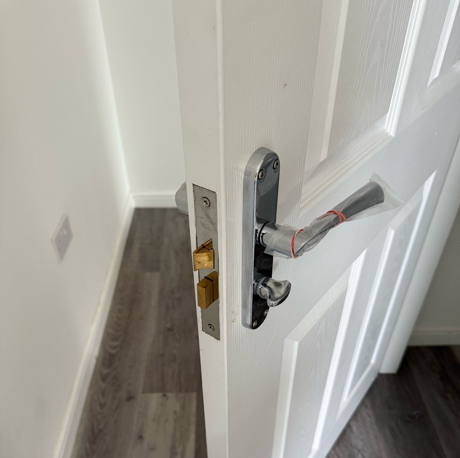 White door with silver handle and lock, partially open in a room with gray flooring and white walls.