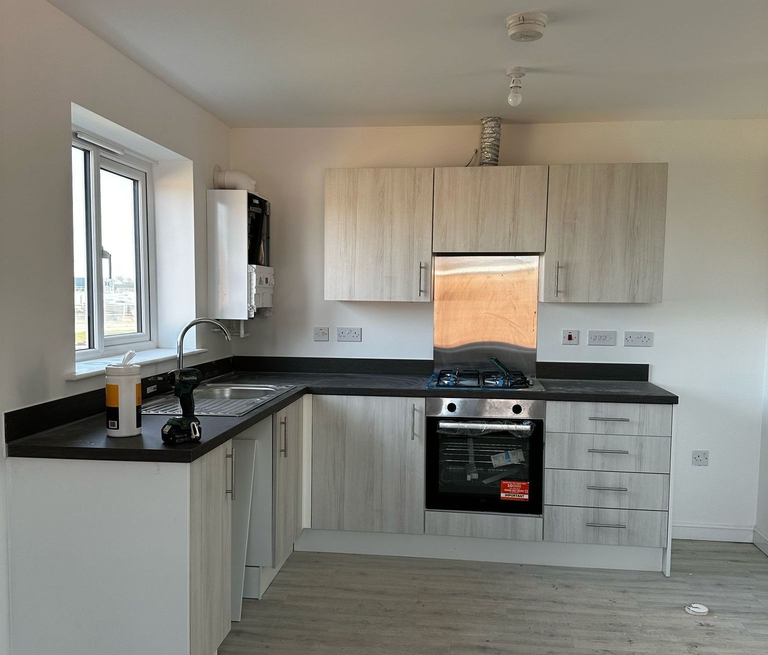 L-shaped kitchen with light wood-look cabinets, dark countertops, and a built-in oven and stovetop.