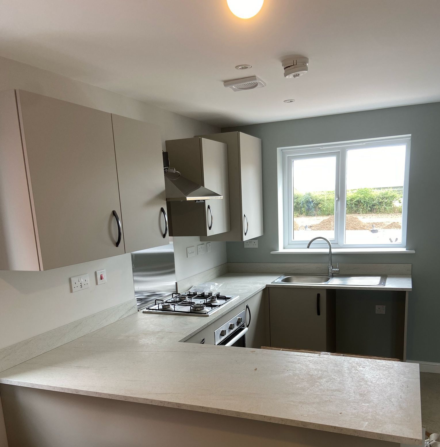 Modern kitchen with light gray cabinets, countertop, and blue-gray walls; a window and appliances are also present.