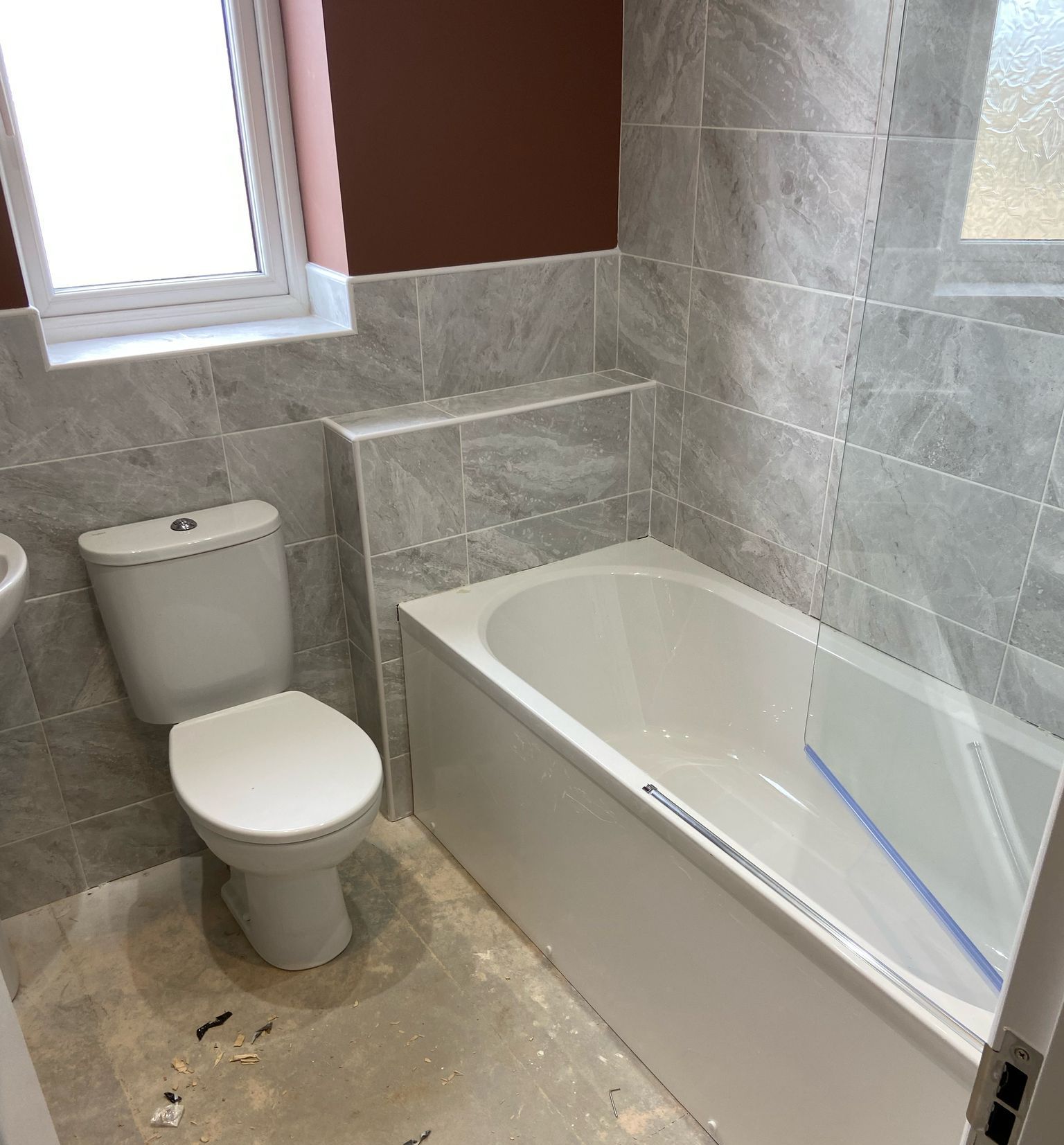 Bathroom with a toilet, bathtub, and tiled walls. A window is visible.