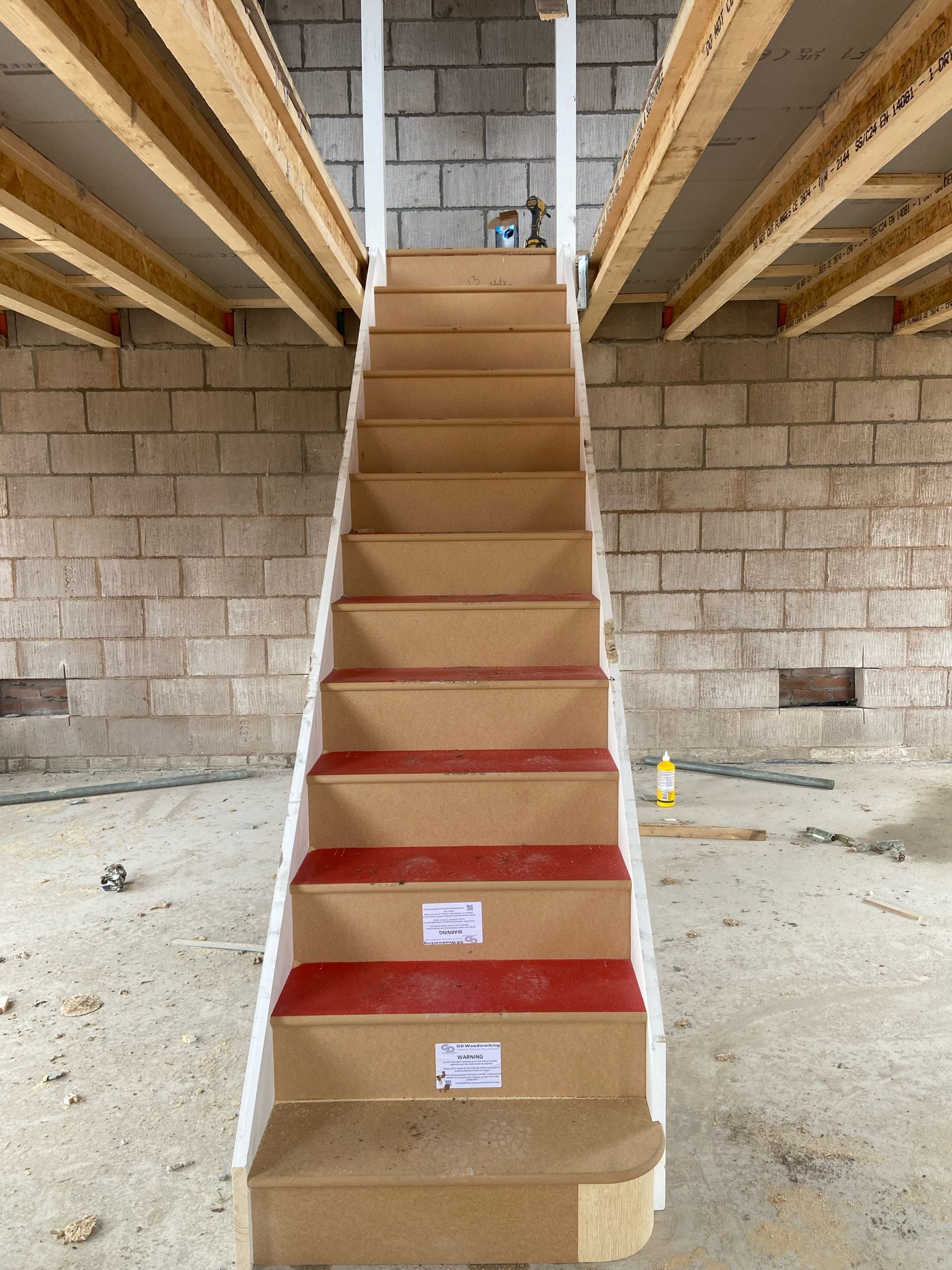 Staircase in a construction setting with beige steps and red edges, leading upward, set between brick walls.