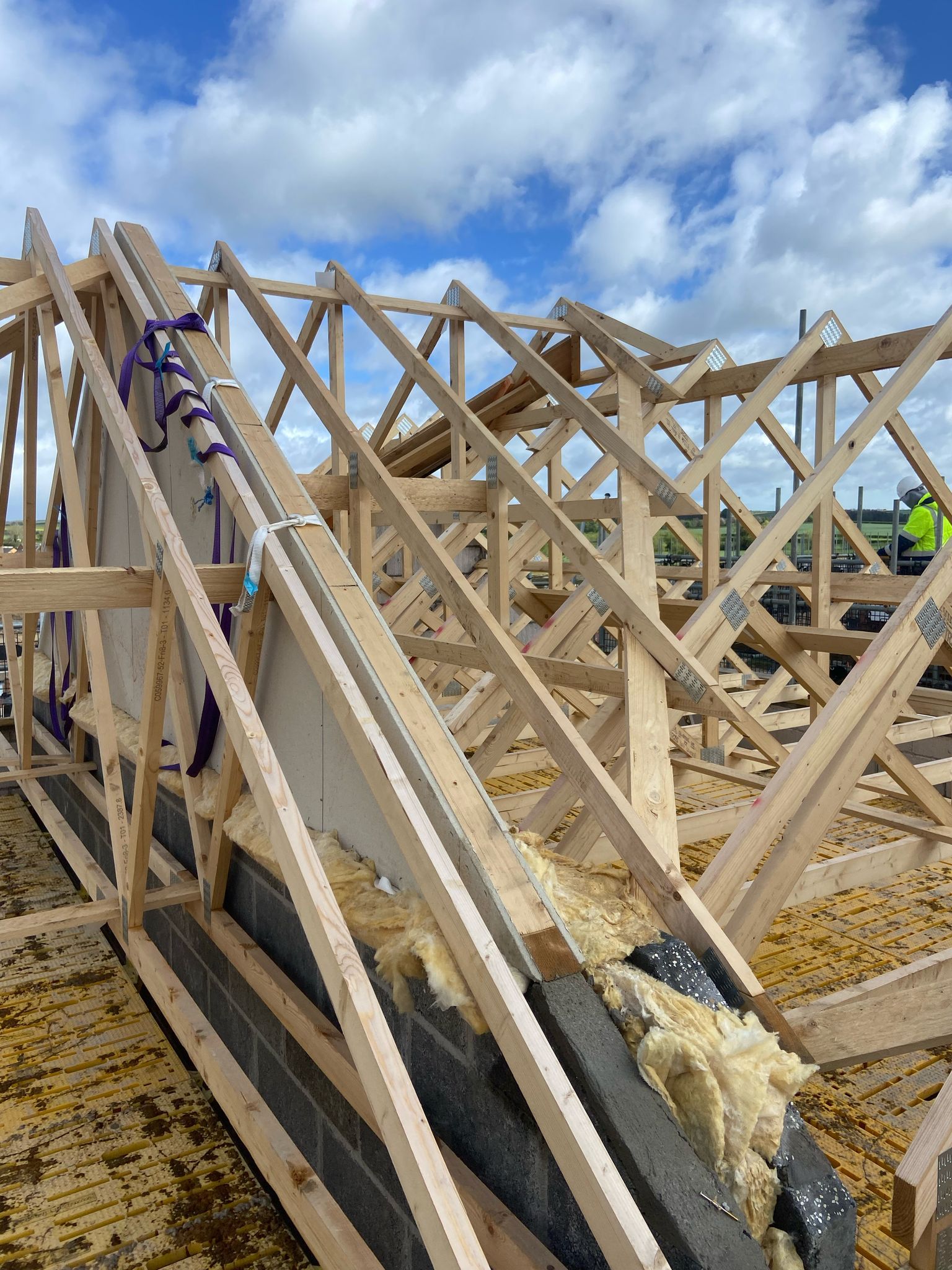 Wooden roof trusses under construction on a brick structure, against a cloudy sky.