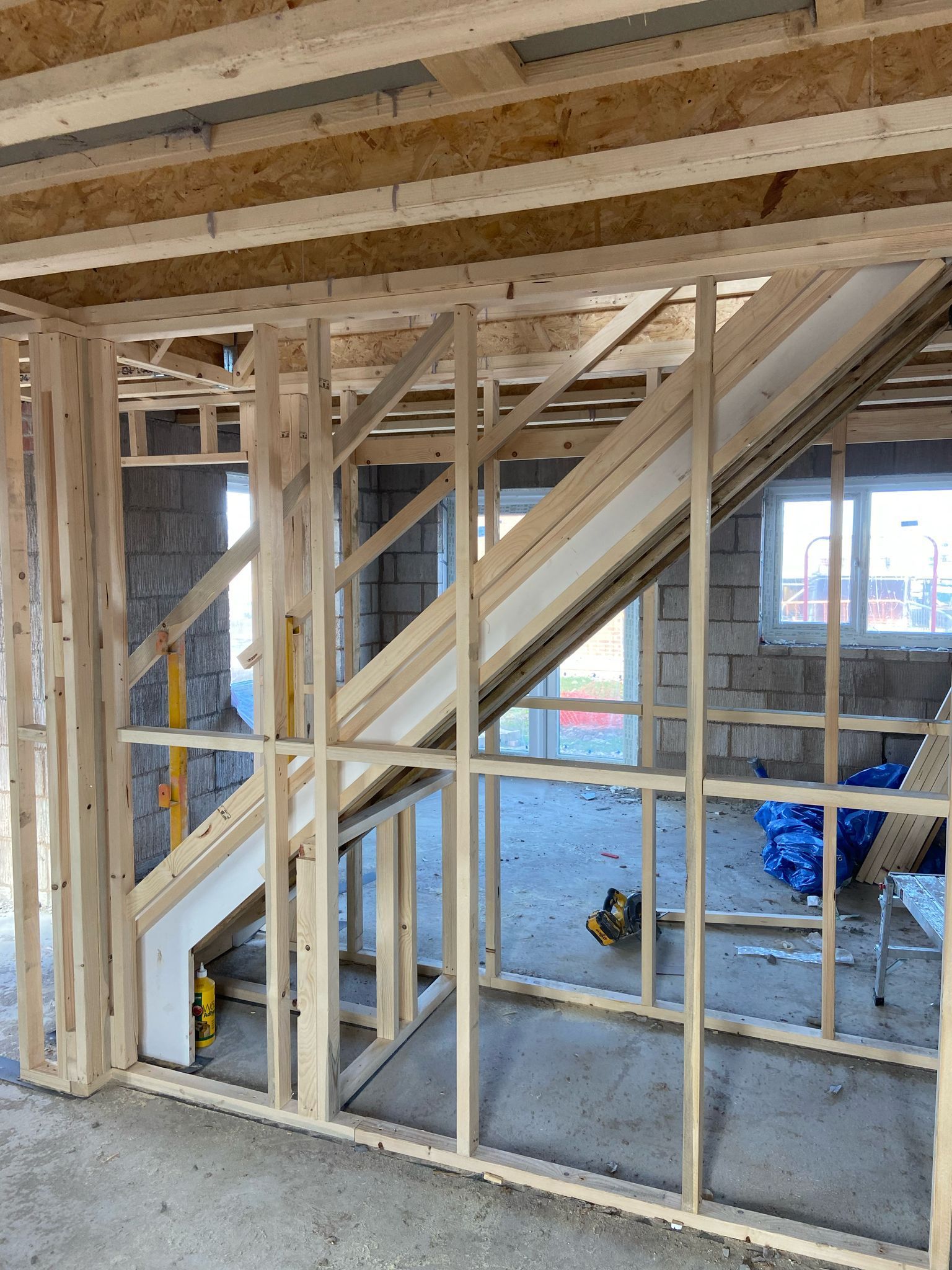 Interior view of a building under construction, showing a wooden staircase frame and wall studs.