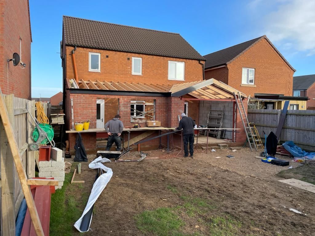 Two men building a brick extension on the back of a two-story house.