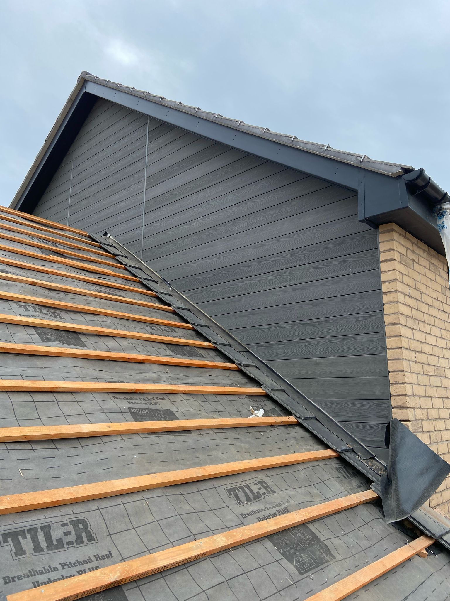 Roof of a house under construction with exposed wooden beams, black underlayment, and a brick chimney.