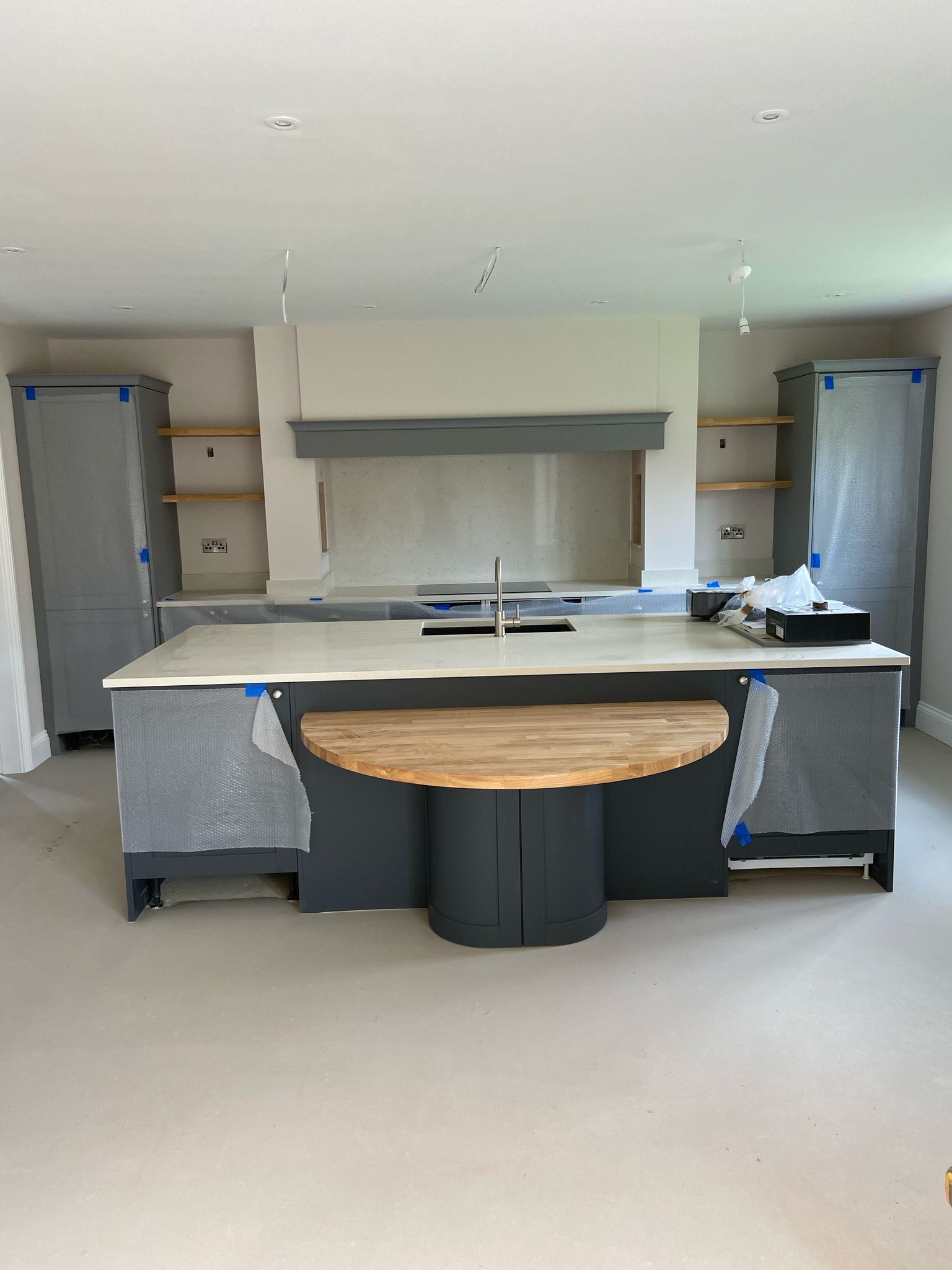 Gray and white kitchen under construction; island with wood table, cabinets covered in plastic.